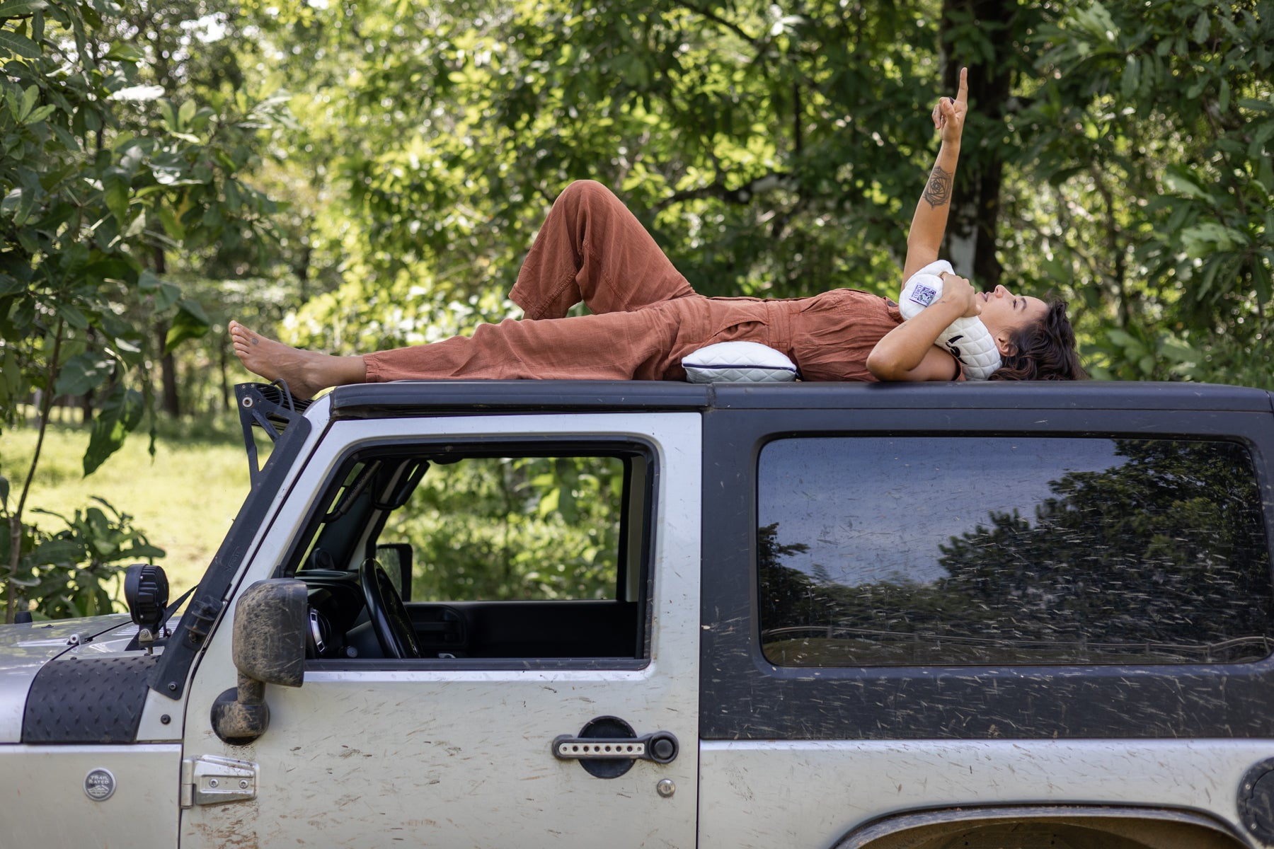 Person lying on the roof of a Jeep with trees in the background